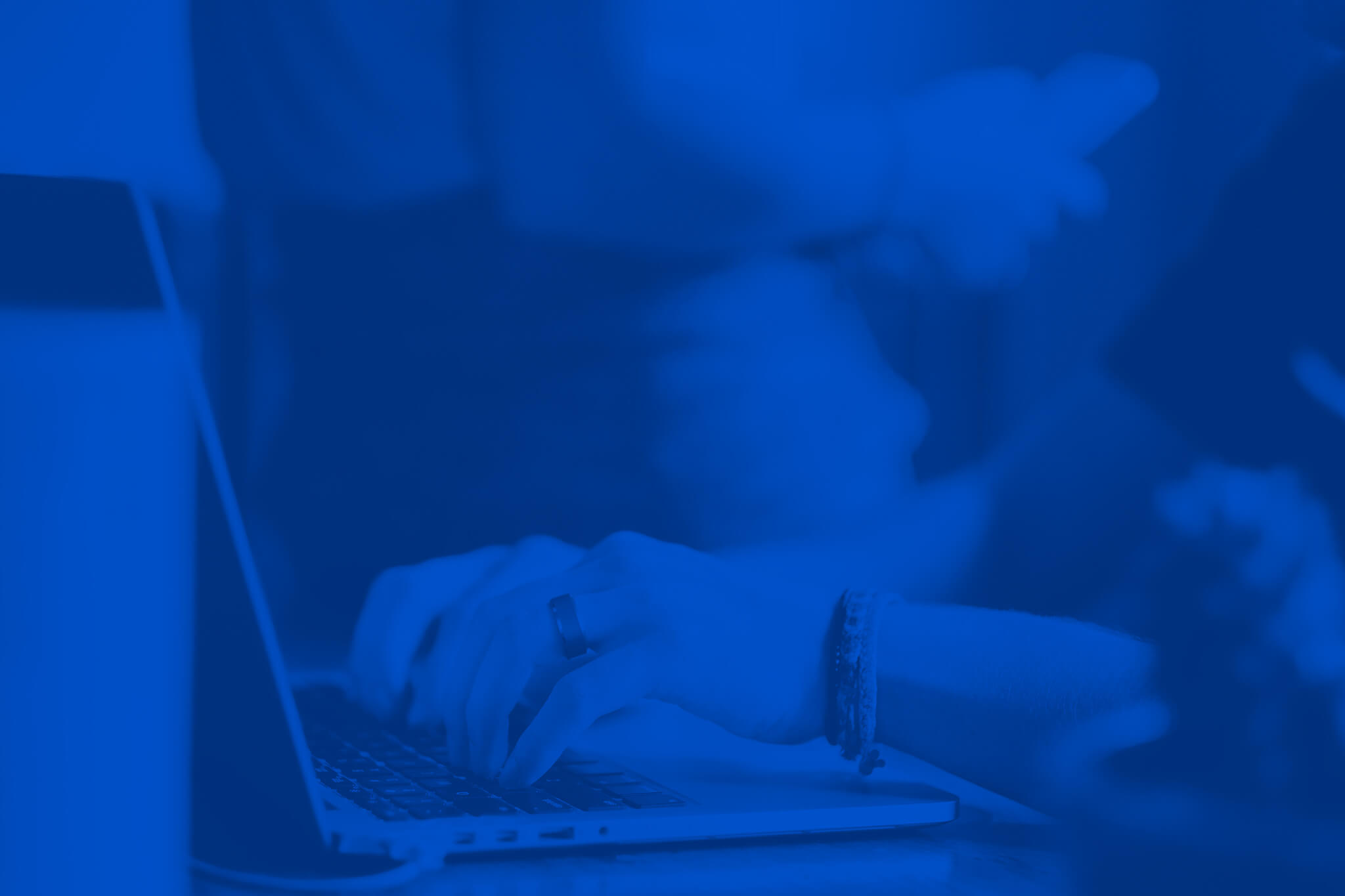 Imagem de fundo, uma mão sobre um teclado de notebook em tons monocromáticos de azul.